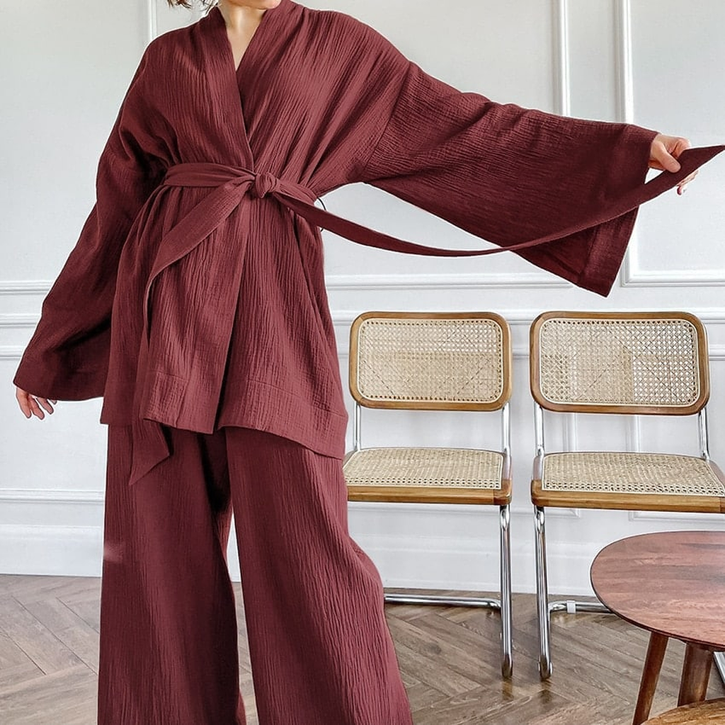 Pyjama kimono rouge bordeaux porté dans un salon, une manche large déployée à bout de bras
