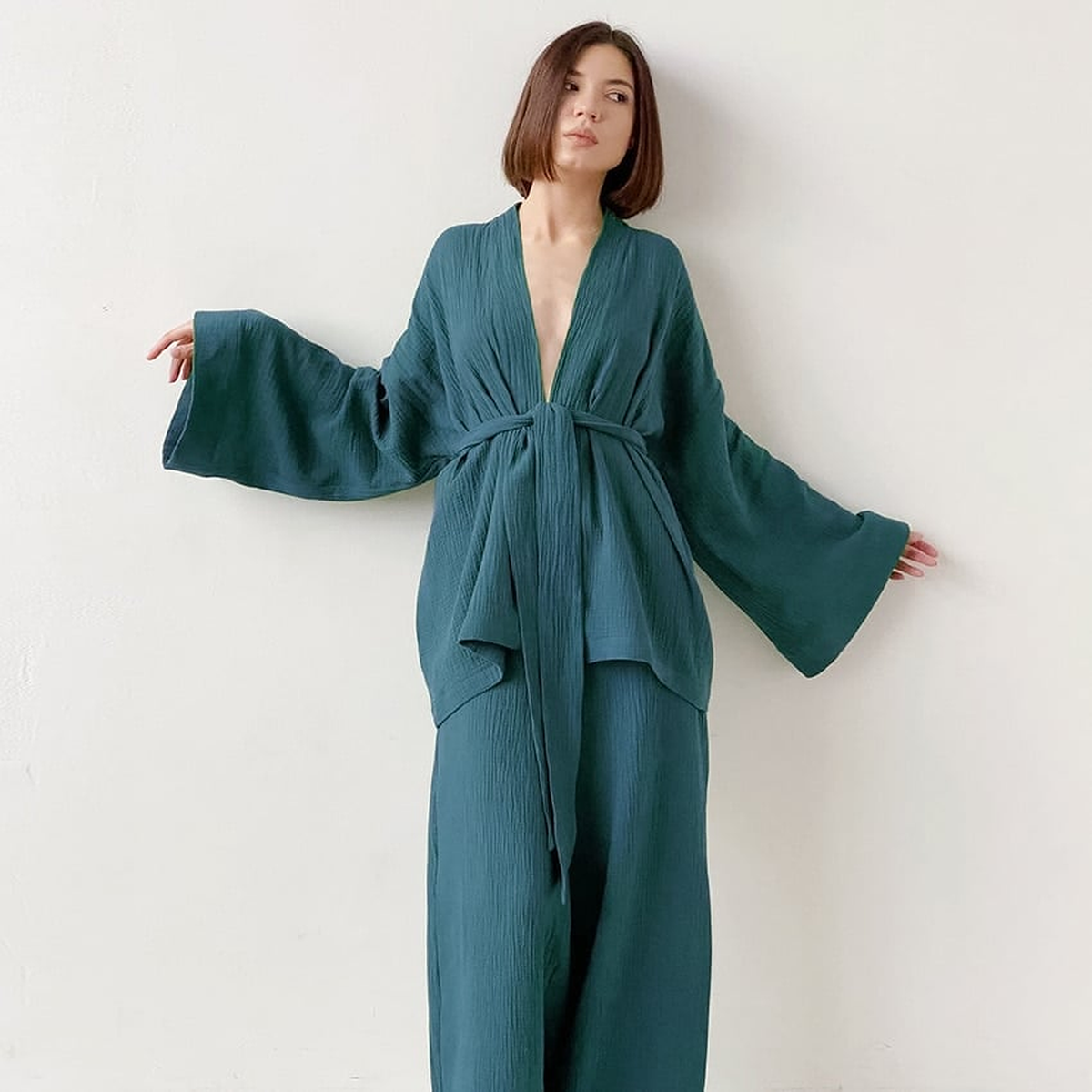Pyjama kimono bleu canard porté contre un mur blanc, les bras écartés, manches déployées