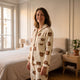 Femme portant le pyjama nounours écru, debout dans une chambre claire, col et poche visibles.