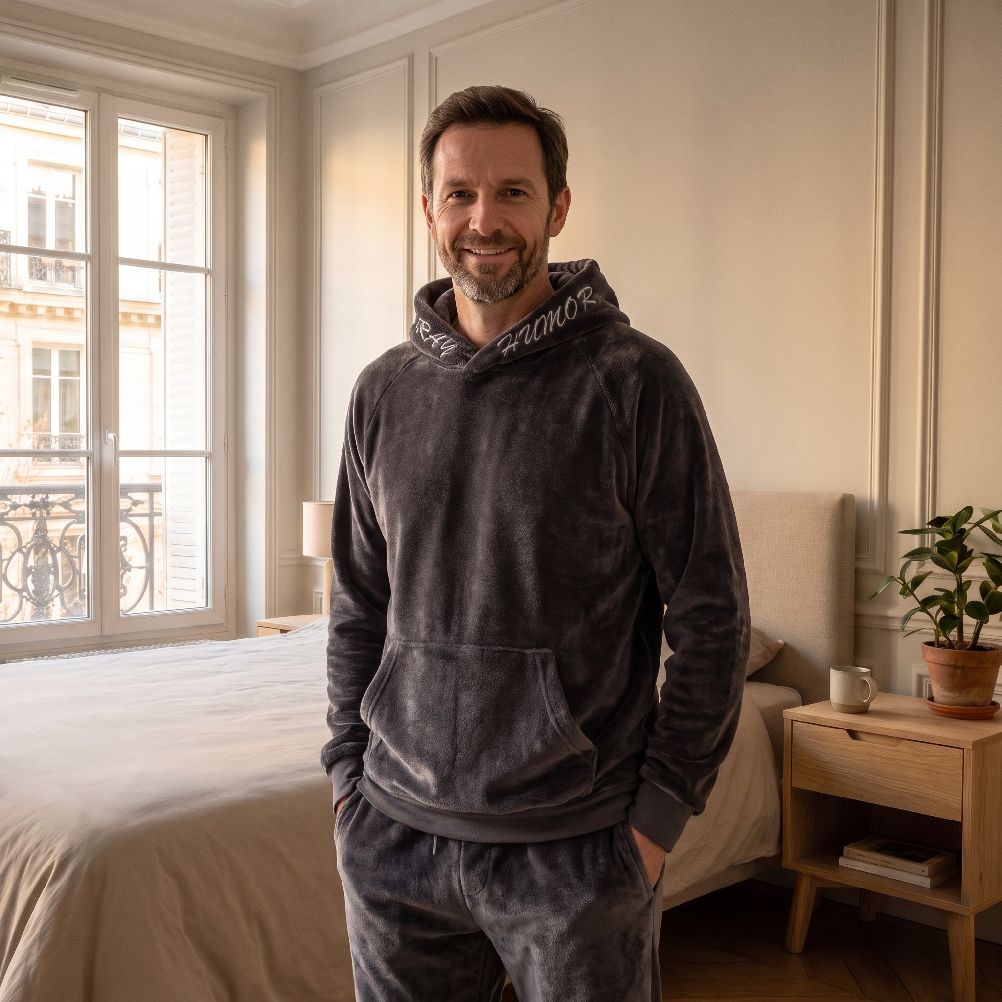 Pyjama polaire gris à capuche porté par un homme debout, les mains dans la poche ventrale, dans une chambre Image