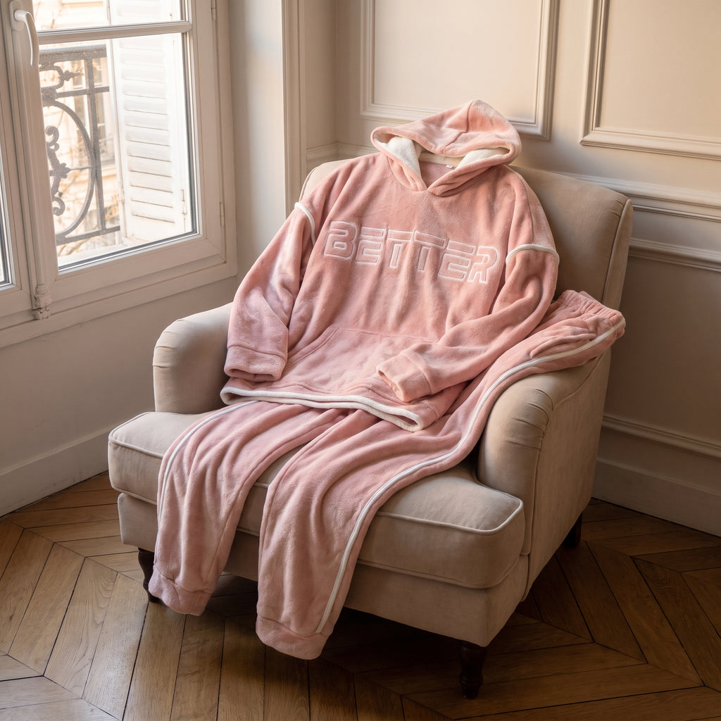 Ensemble deux pièces du pyjama polaire rose posé sur un fauteuil : haut à capuche et pantalon à liseré blanc