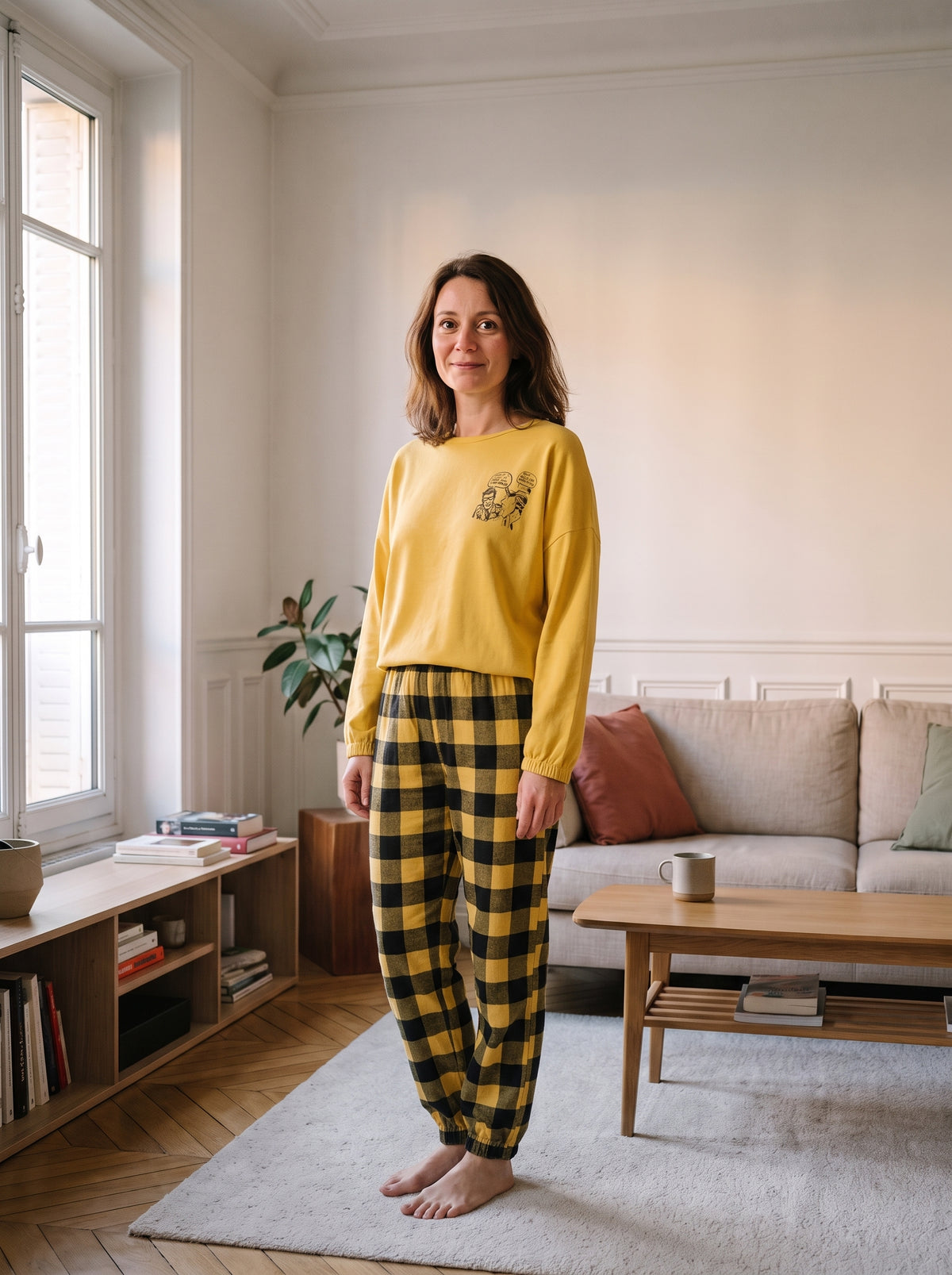 Pyjama femme jaune moutarde porté debout dans un salon, haut uni et pantalon à carreaux