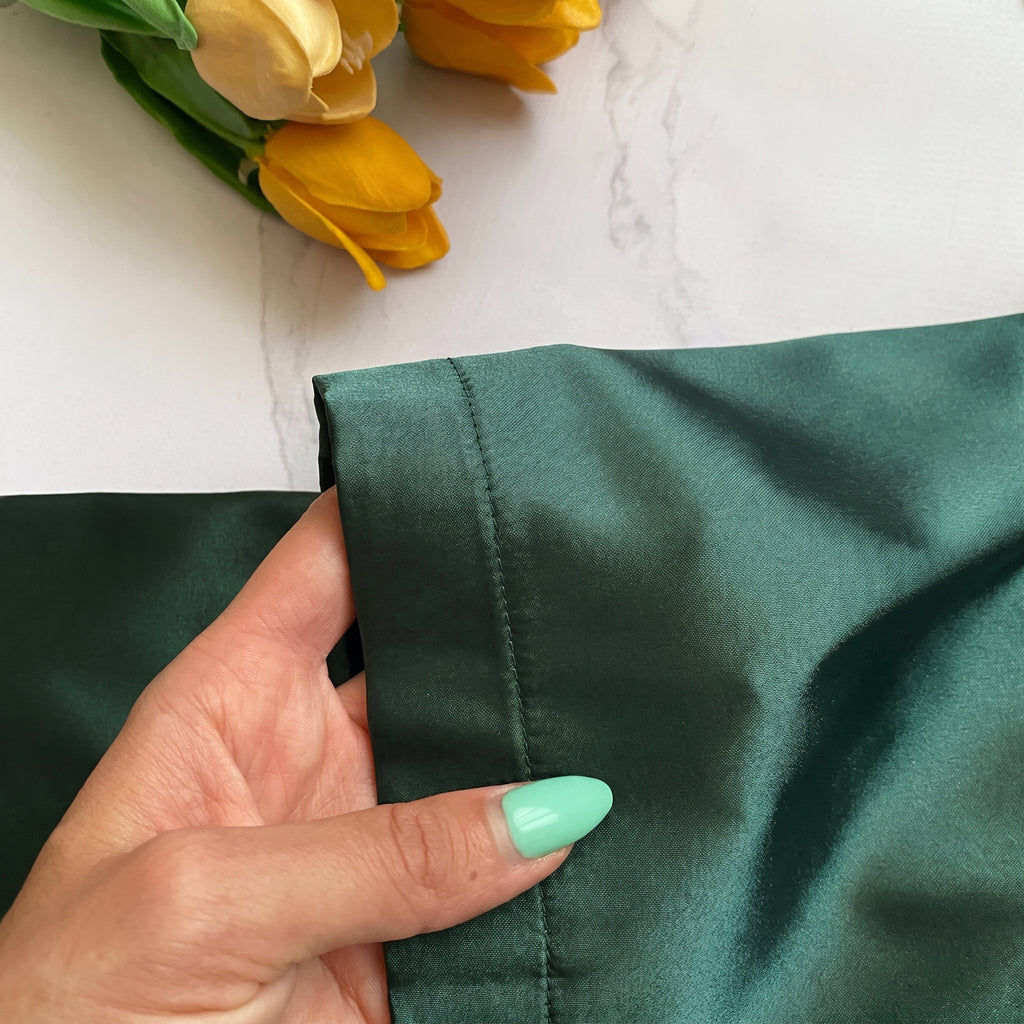 Détail du satin vert foncé et de la couture fine au bord de la manche évasée