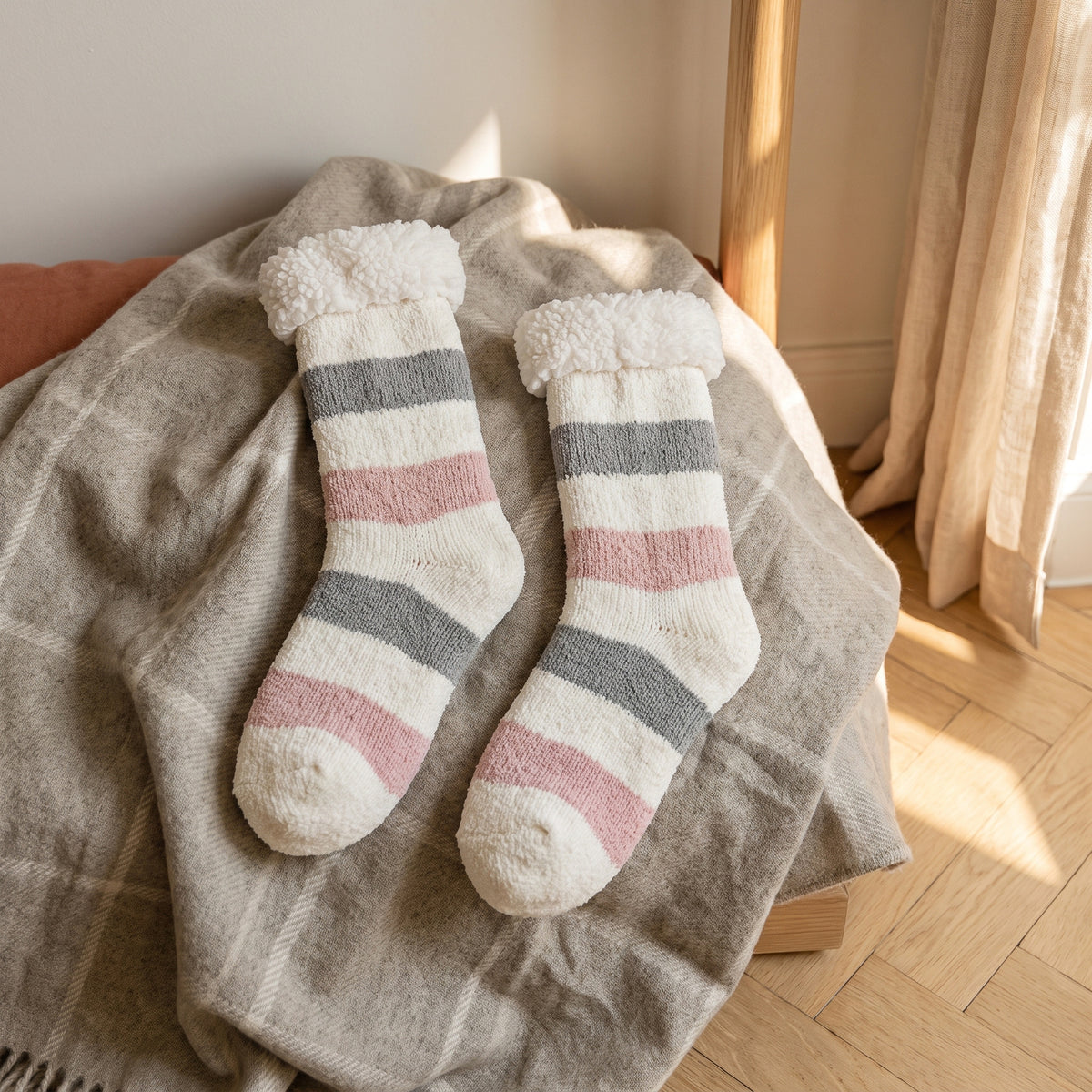 Paire de chaussettes fourrées à rayures grises et roses posée à plat sur un plaid, revers déployé