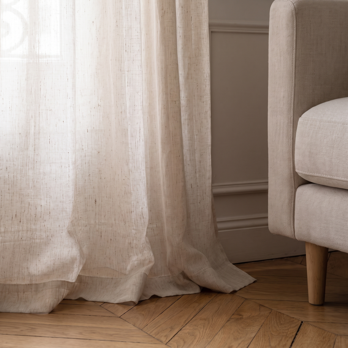 Ourlet et retombée au sol d’un pan du rideau voilage en tulle beige Image