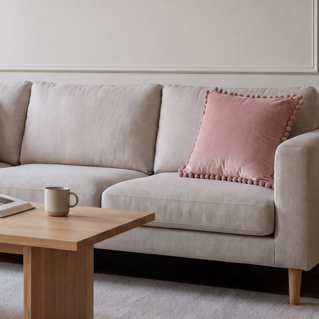 Housse de coussin en velours rose à pompons posée sur un canapé écru