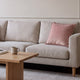 Housse de coussin en velours rose à pompons posée sur un canapé écru