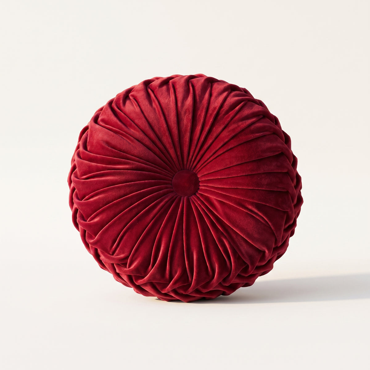 Coussin rond plissé en velours rouge, vue de face sur fond neutre