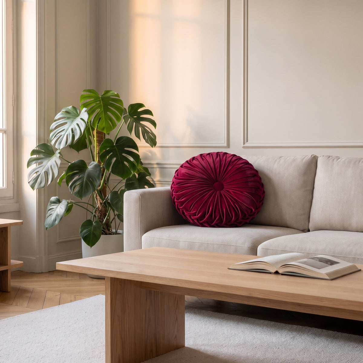Coussin rond plissé en velours rouge, posé dans l'angle d'un canapé clair