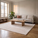 Tapis en fausse fourrure beige déroulé devant un canapé clair, sur un parquet en point de Hongrie
