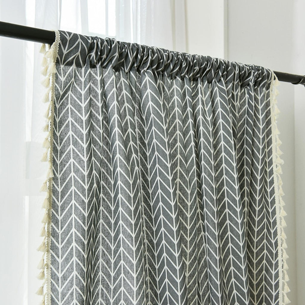 Gros plan sur le motif chevron gris bleuté du rideau, bordé de pompons écrus