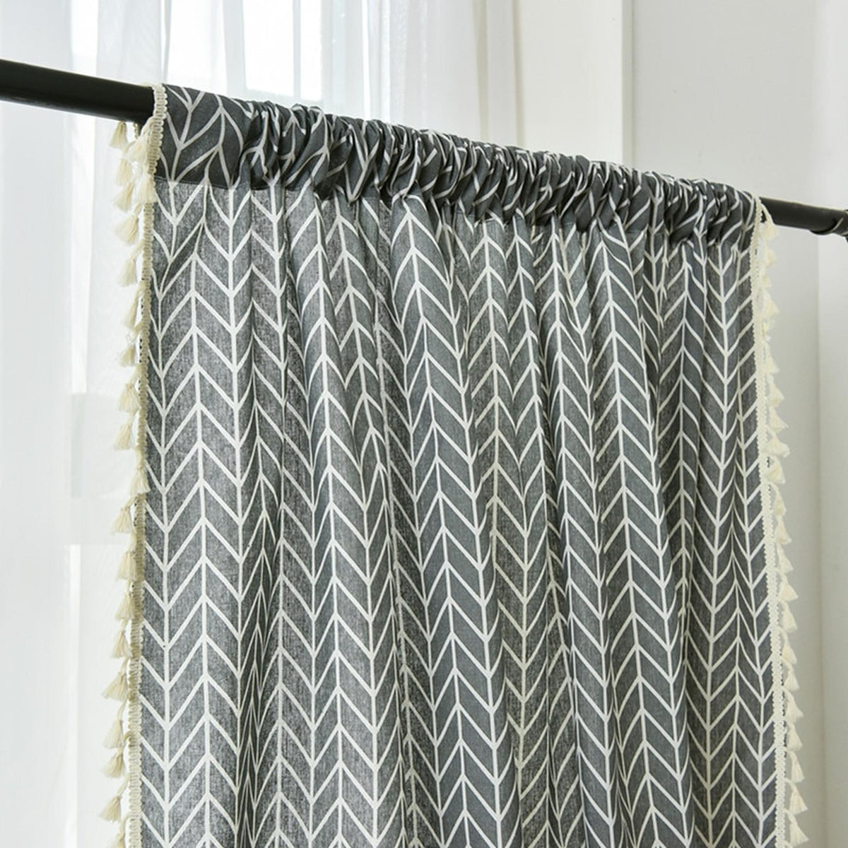 Gros plan sur le motif chevron gris bleuté du rideau, bordé de pompons écrus