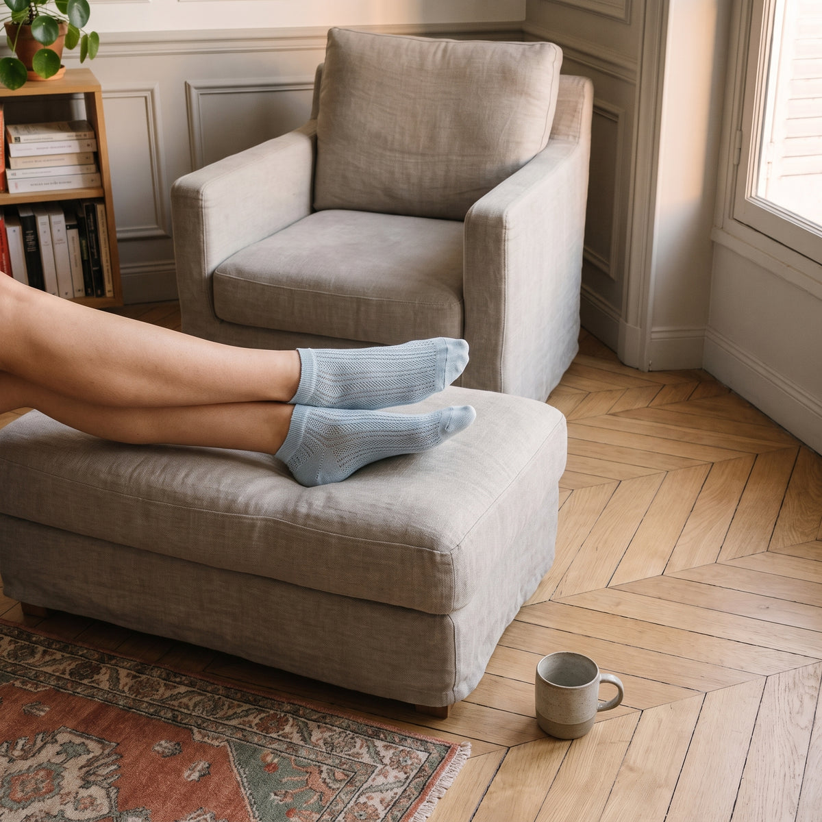Pieds en socquettes bleu ciel posés sur le repose-pieds d'un coin lecture, près de la fenêtre Image