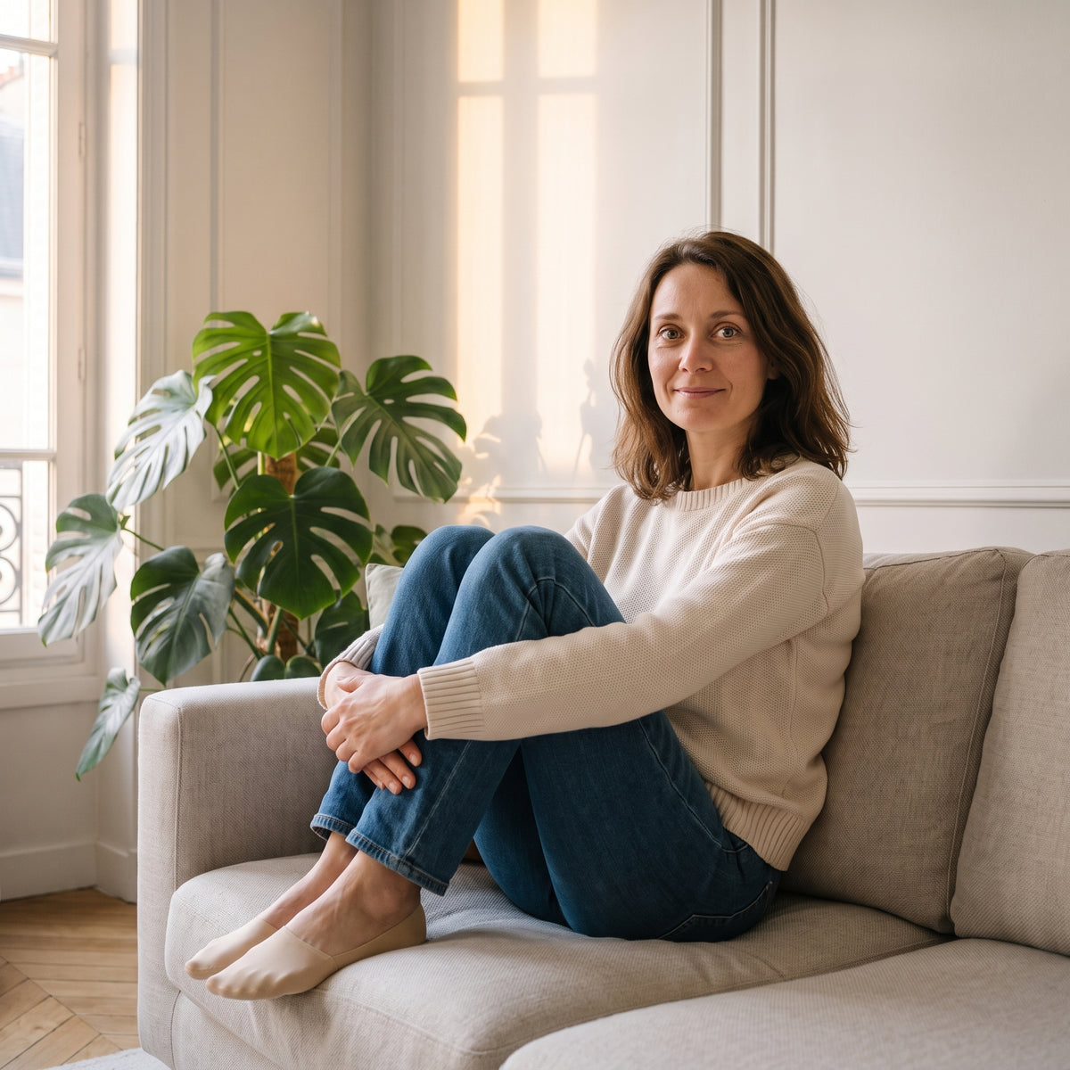 Femme assise sur son canapé, genoux repliés, en socquettes invisibles beige nu