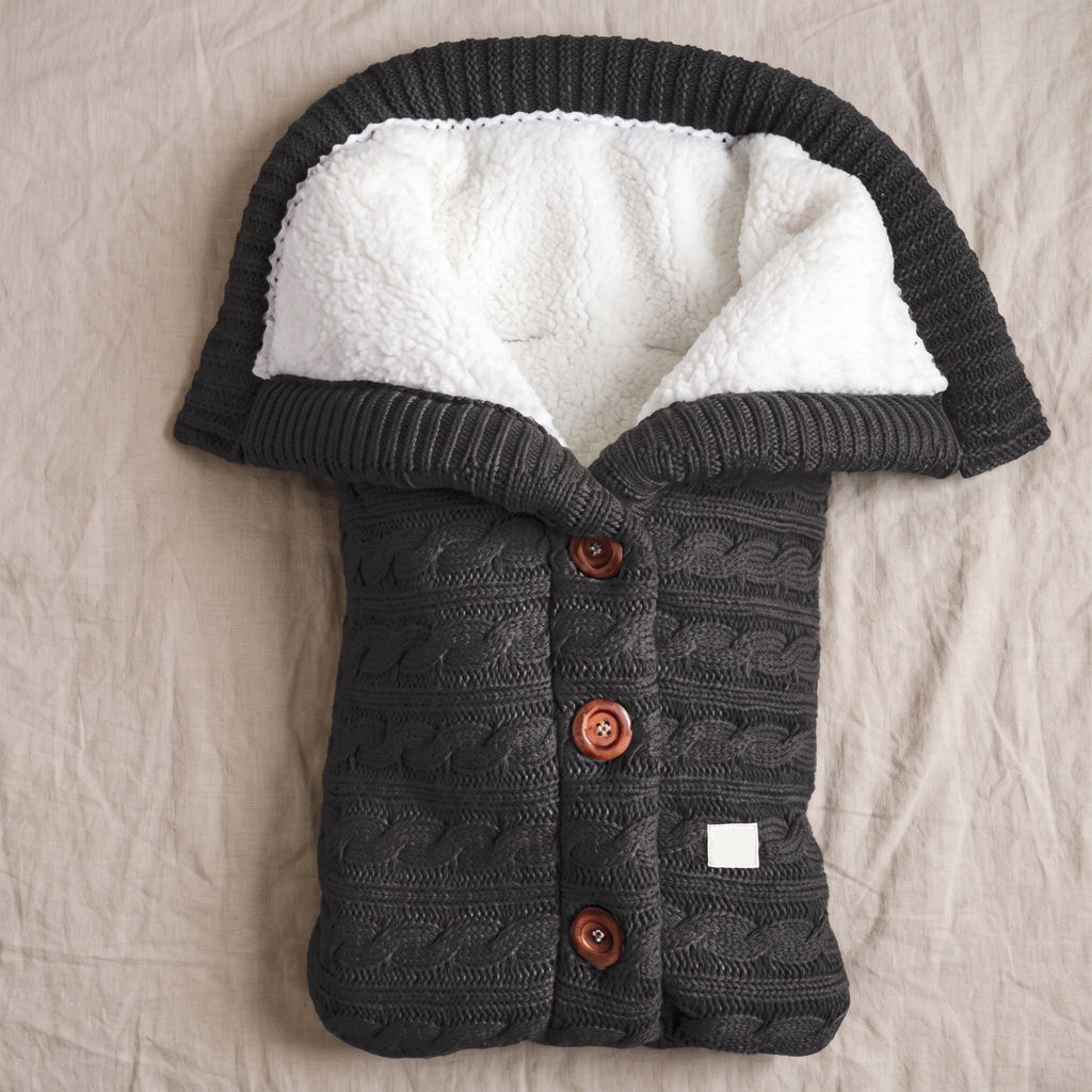 Nid d’ange bébé noir tricoté posé à plat sur un couvre-lit clair
