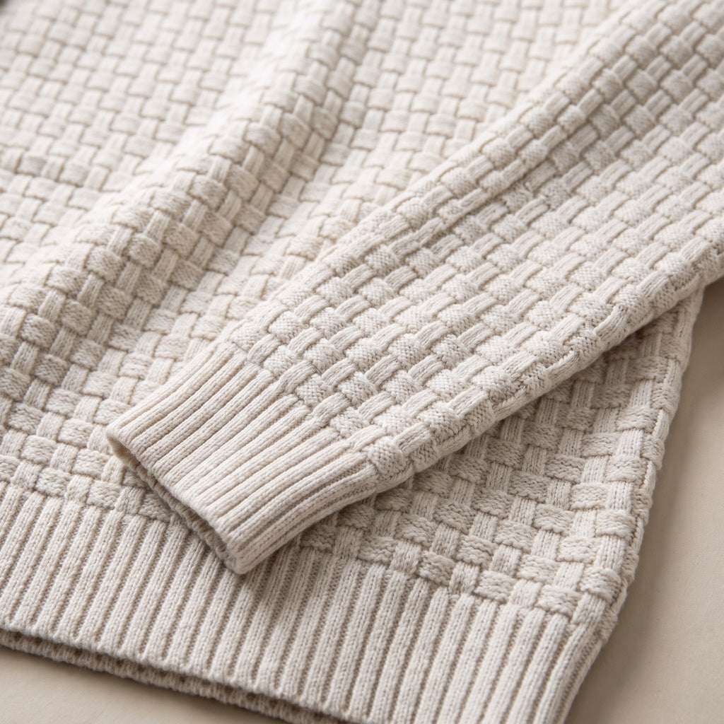 Gros plan sur le bas d'une manche : la maille en damier sur l'avant-bras et la bande de côtes fines et serrées du poignet.
