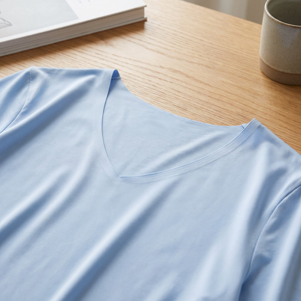 Haut d un t-shirt col V bleu ciel pose a plat sur une table en chene : la pointe du V et le dos de l encolure, ou la maille est nue Image