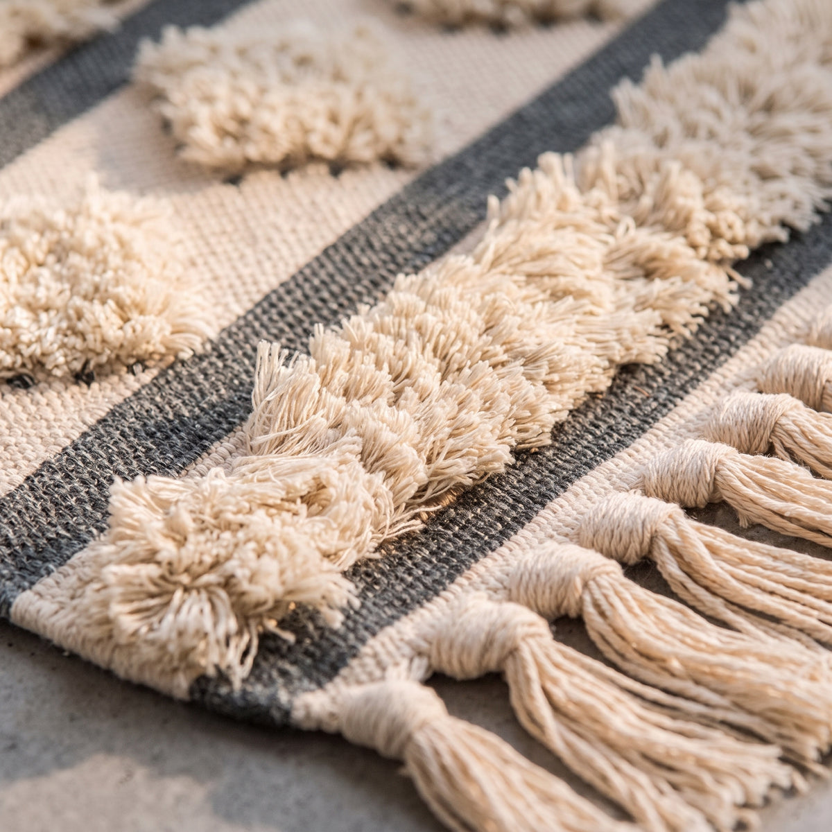Gros plan sur le relief tufté du tapis ethnique, ses boucles de coton écru et sa bande tissée gris anthracite Image