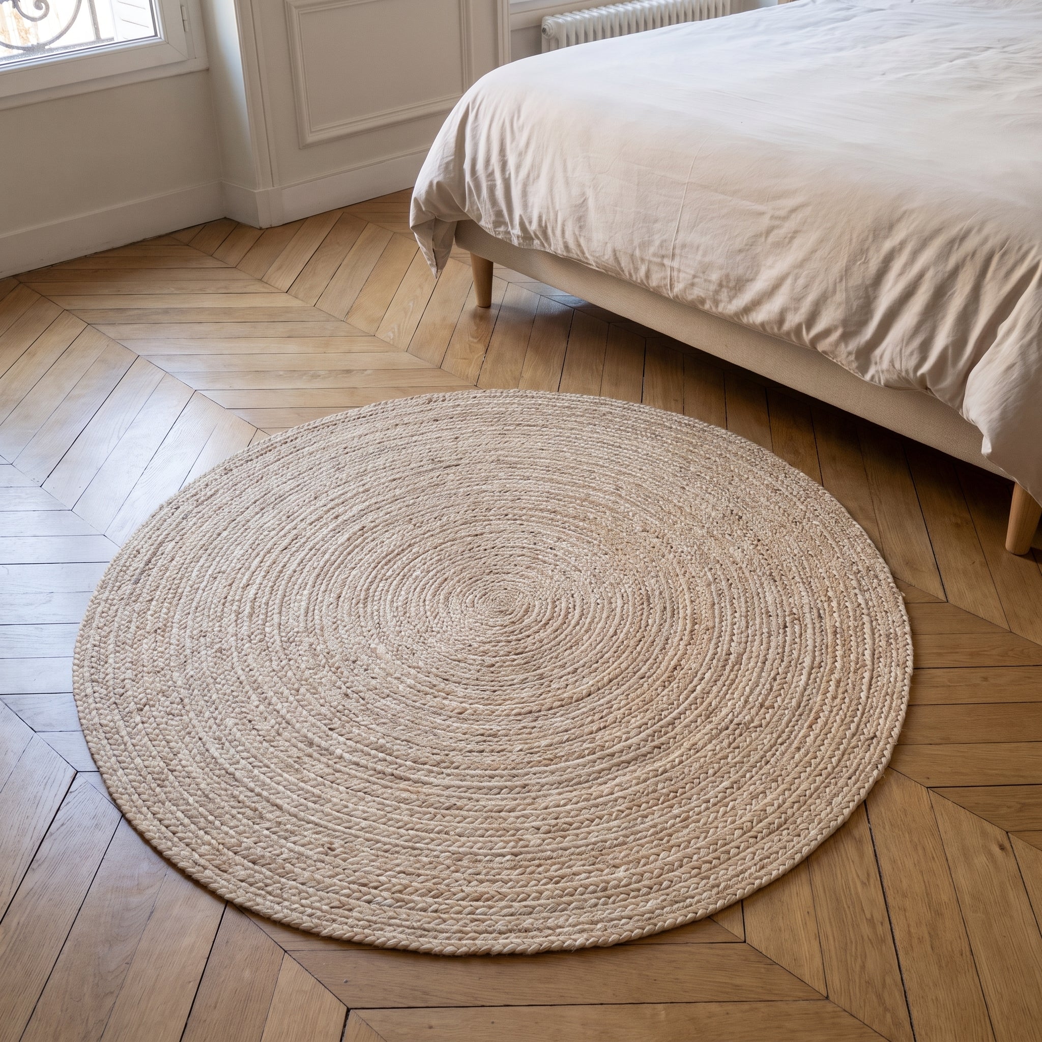 Tapis rond en sisal beige posé à plat sur un parquet, au pied d'un lit Image