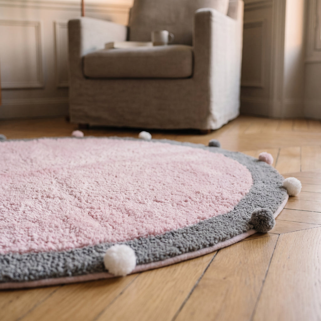 Gros plan sur le duvet moelleux et la bordure à pompons du tapis rond rose