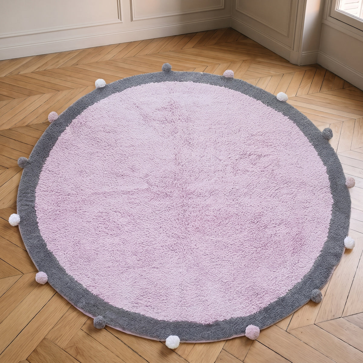 Tapis rond à pompons rose vu de dessus, posé à plat sur le sol d'une pièce claire, le cercle entier dans le cadre