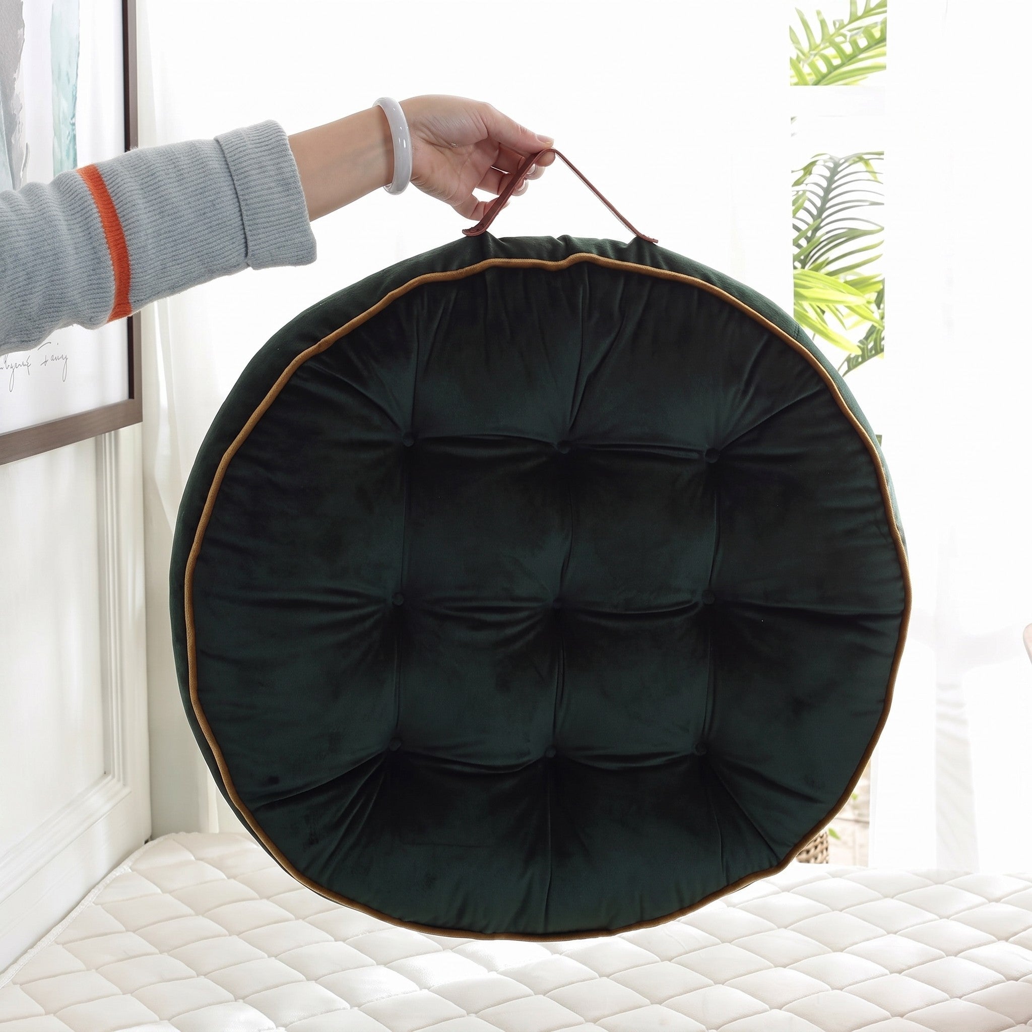 Main tenant le coussin de sol rond vert par son anse en simili cuir Image
