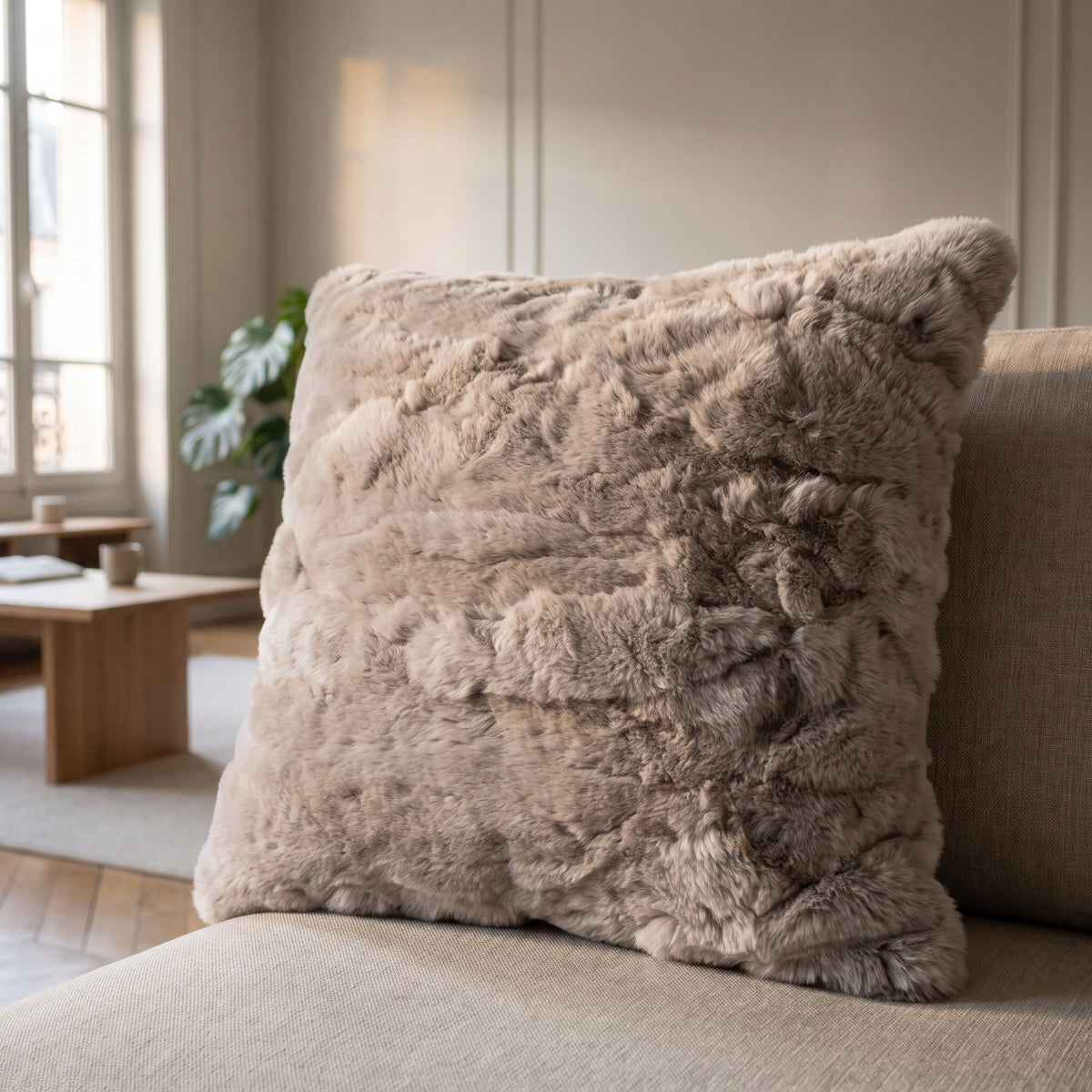 Coussin extra doux en fausse fourrure taupe posé sur l'assise d'un canapé en lin clair