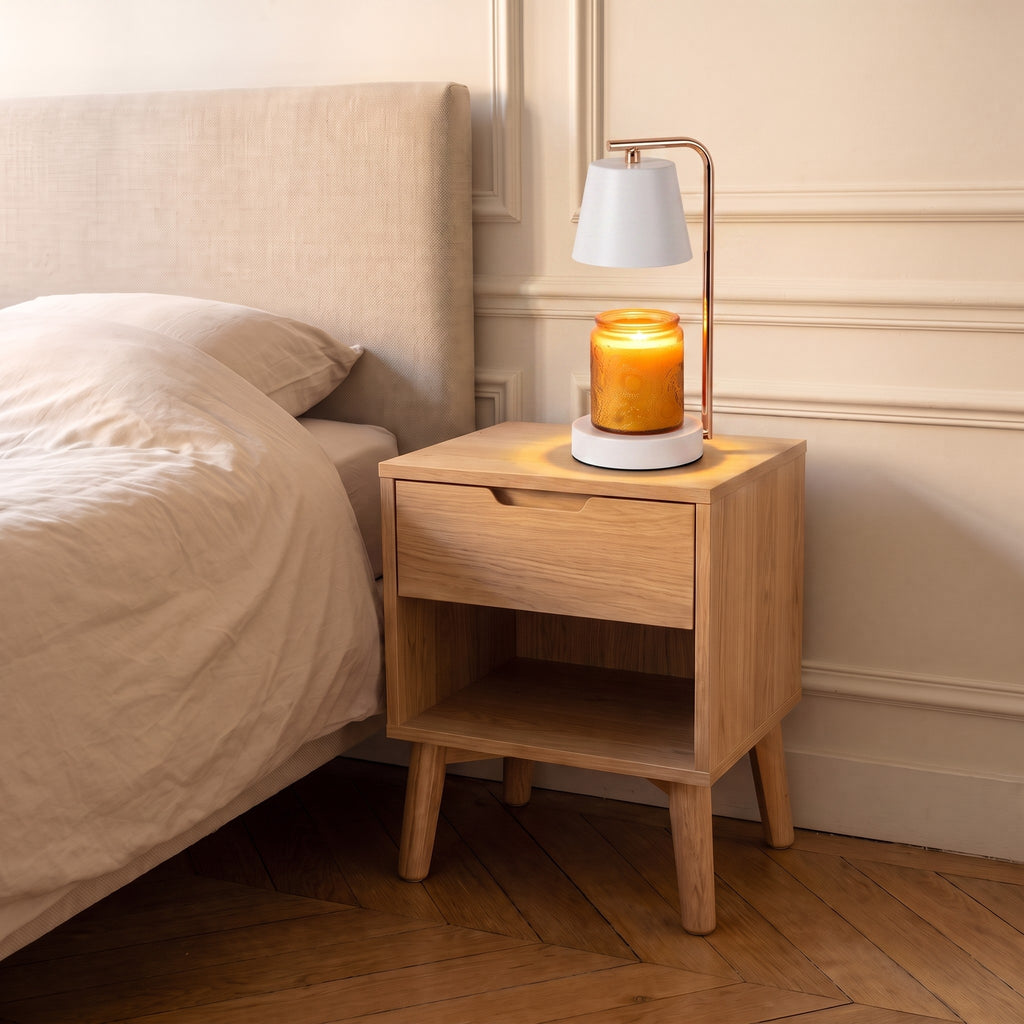 Lampe chauffe-bougie blanche allumée sur une table de chevet, le pot de bougie éclairé par-dessous