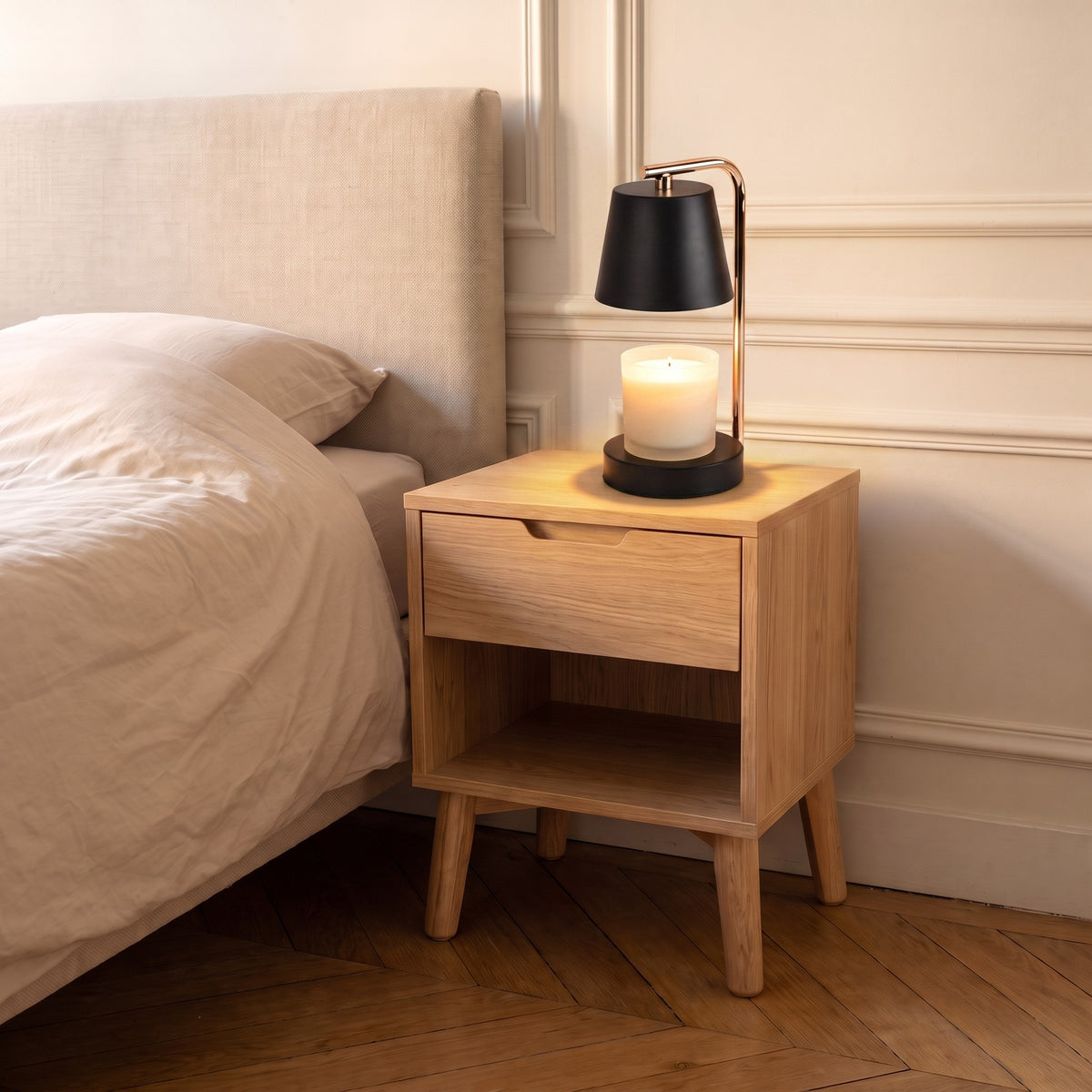 Lampe chauffe-bougie noire allumée sur une table de chevet, la cire du pot de bougie fond sous l'abat-jour