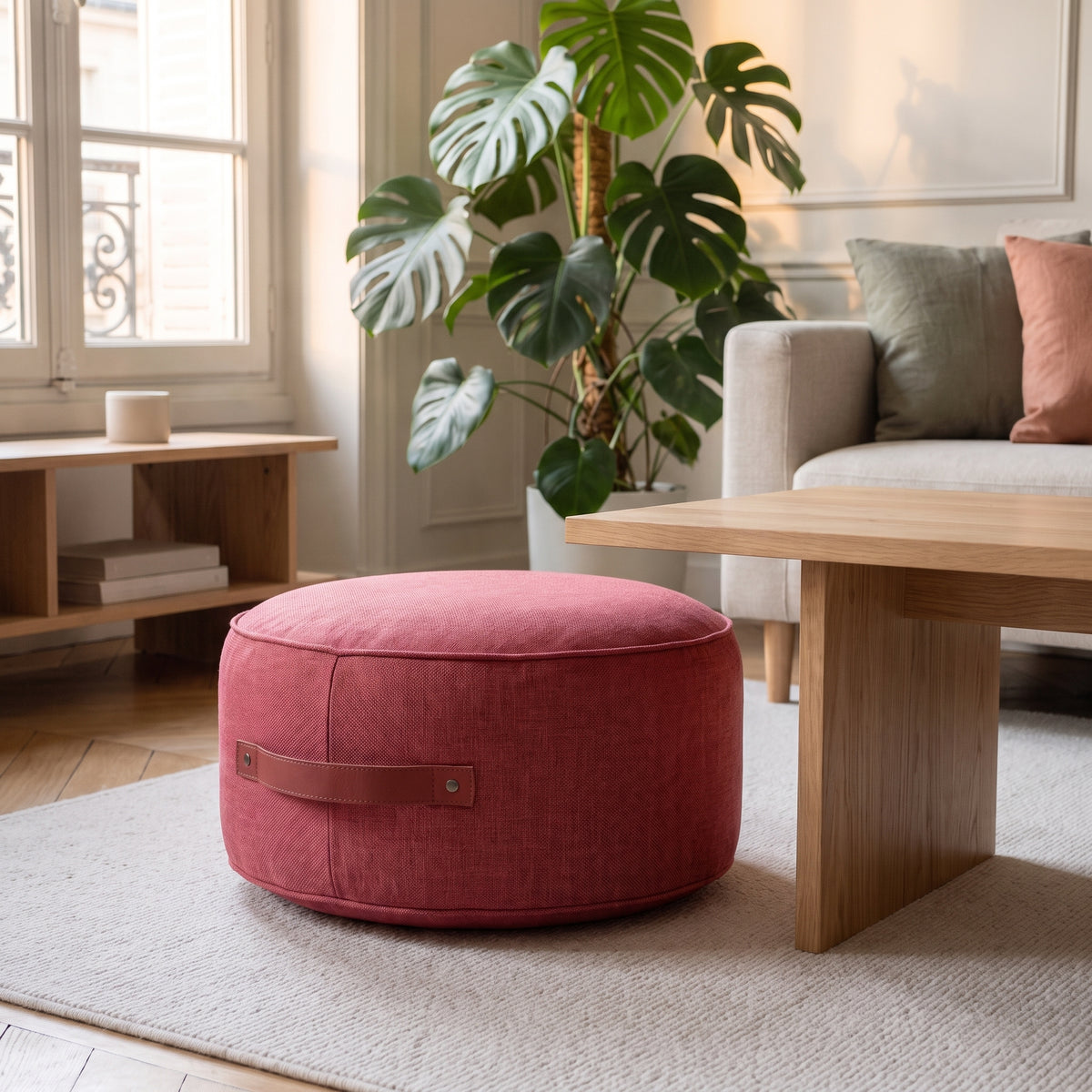 Pouf de sol rond framboise posé sur le tapis du salon, poignée visible