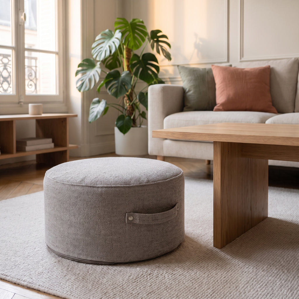 Pouf de sol rond gris chiné posé sur le tapis du salon, poignée visible