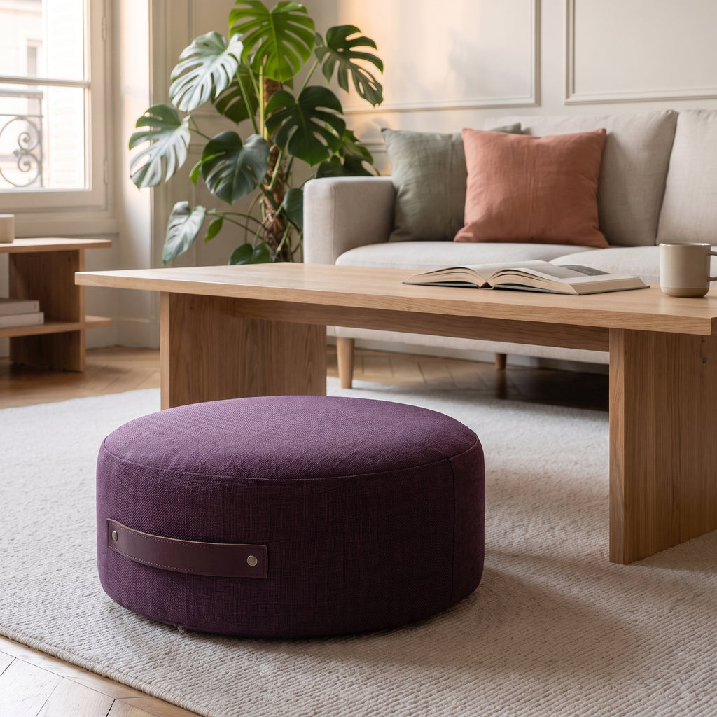 Pouf de sol rond prune posé sur le tapis du salon, poignée visible