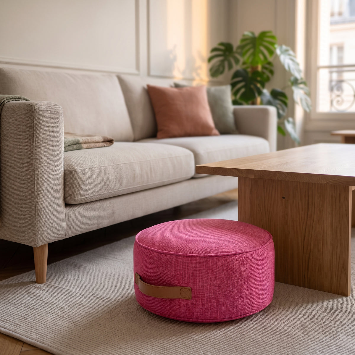 Pouf de sol rond rose vif posé sur le tapis du salon, poignée visible