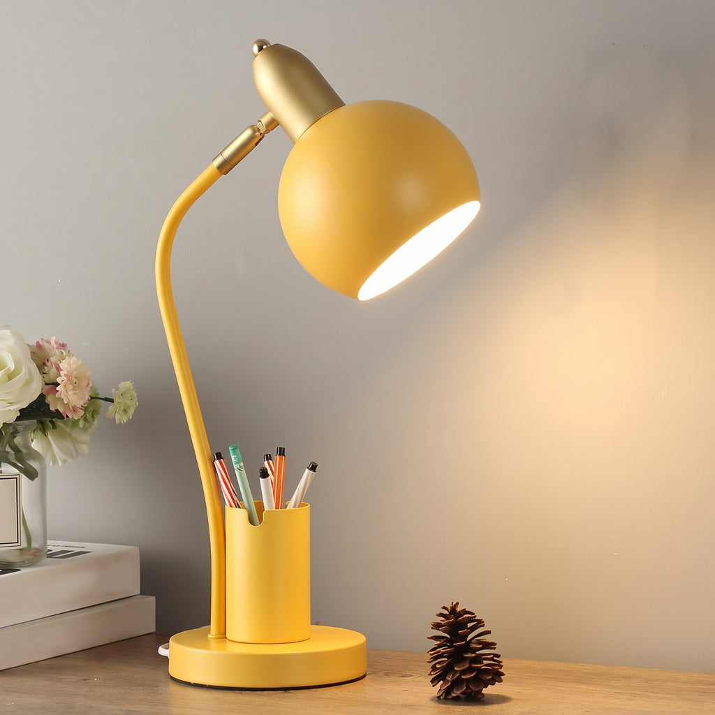 Lampe de bureau à pot à crayons, coloris jaune moutarde, allumée sur un bureau en bois
