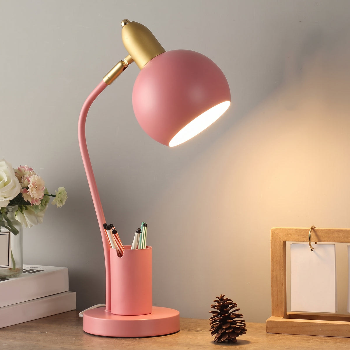 Lampe de bureau à pot à crayons, coloris rose corail, allumée sur un bureau en bois