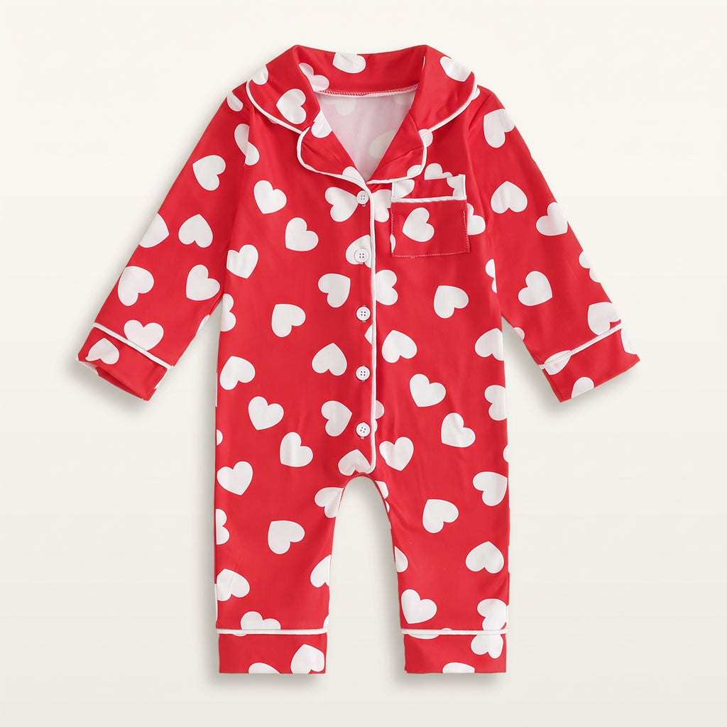 Combinaison pyjama bébé rouge à cœurs blancs, vue de face sur fond blanc cassé