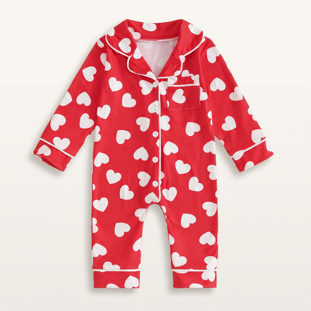 Combinaison pyjama bébé rouge à cœurs blancs, vue de face sur fond blanc cassé