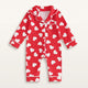 Combinaison pyjama bébé rouge à cœurs blancs, vue de face sur fond blanc cassé