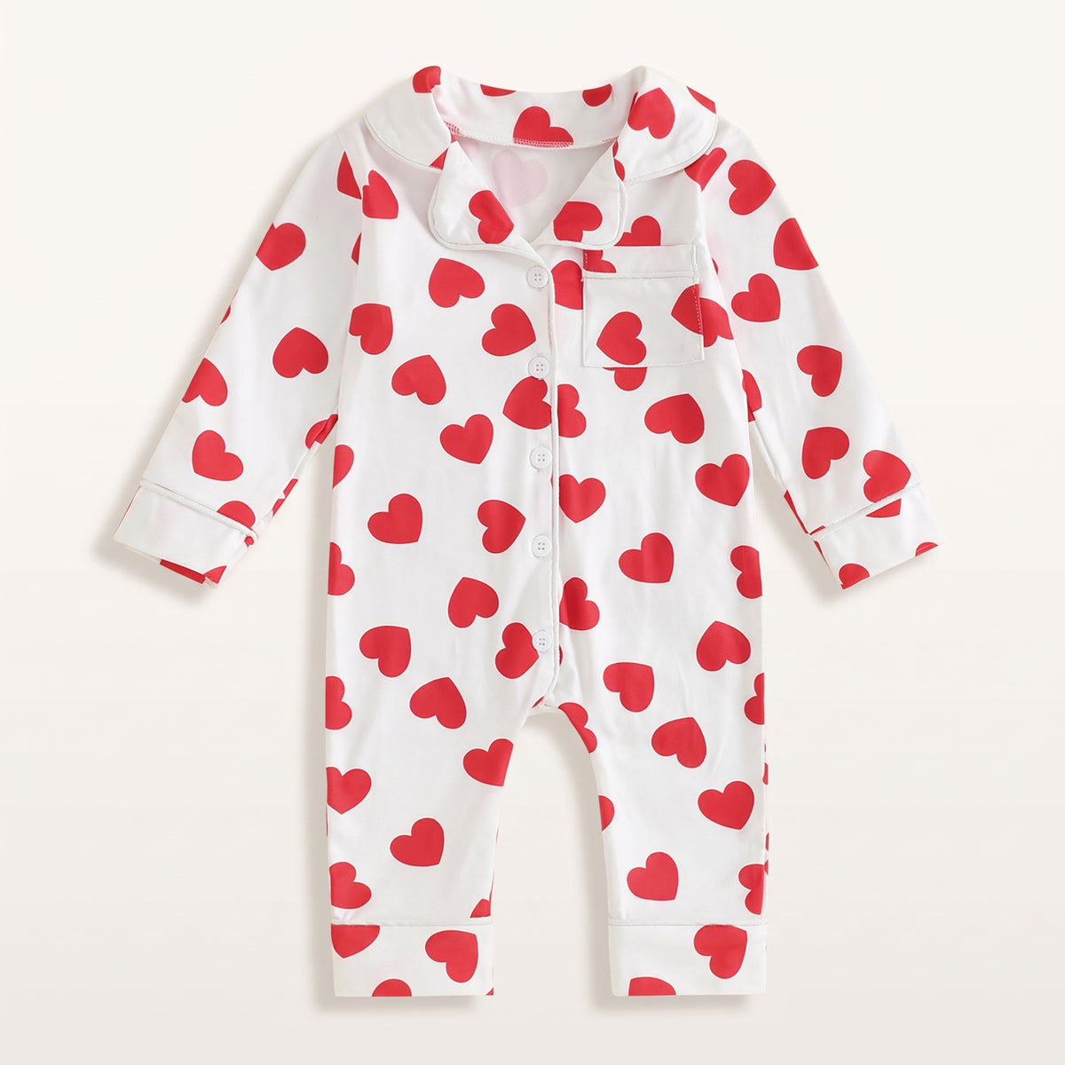 Combinaison pyjama bébé blanche à cœurs rouges, vue de face sur fond blanc cassé