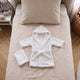 Peignoir de bain bebe blanc a capuche et sa serviette, a plat sur le lit