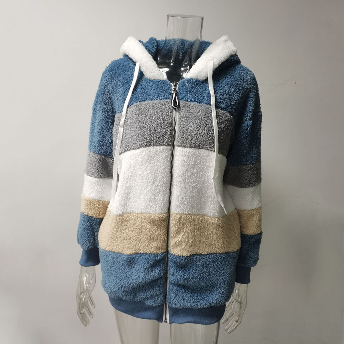Veste bleue en fausse fourrure vue de face sur mannequin transparent, capuche blanche et panneaux gris, blanc et crème