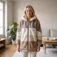 Veste marron en fausse fourrure portée de face dans un intérieur lumineux, capuche blanche et panneaux gris, blanc et crème