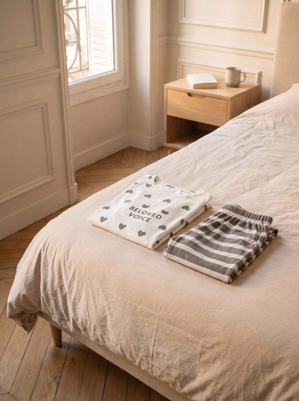 L ensemble pyjama blanc a coeurs plie au pied du lit, le haut et le pantalon raye poses l un sur l autre.