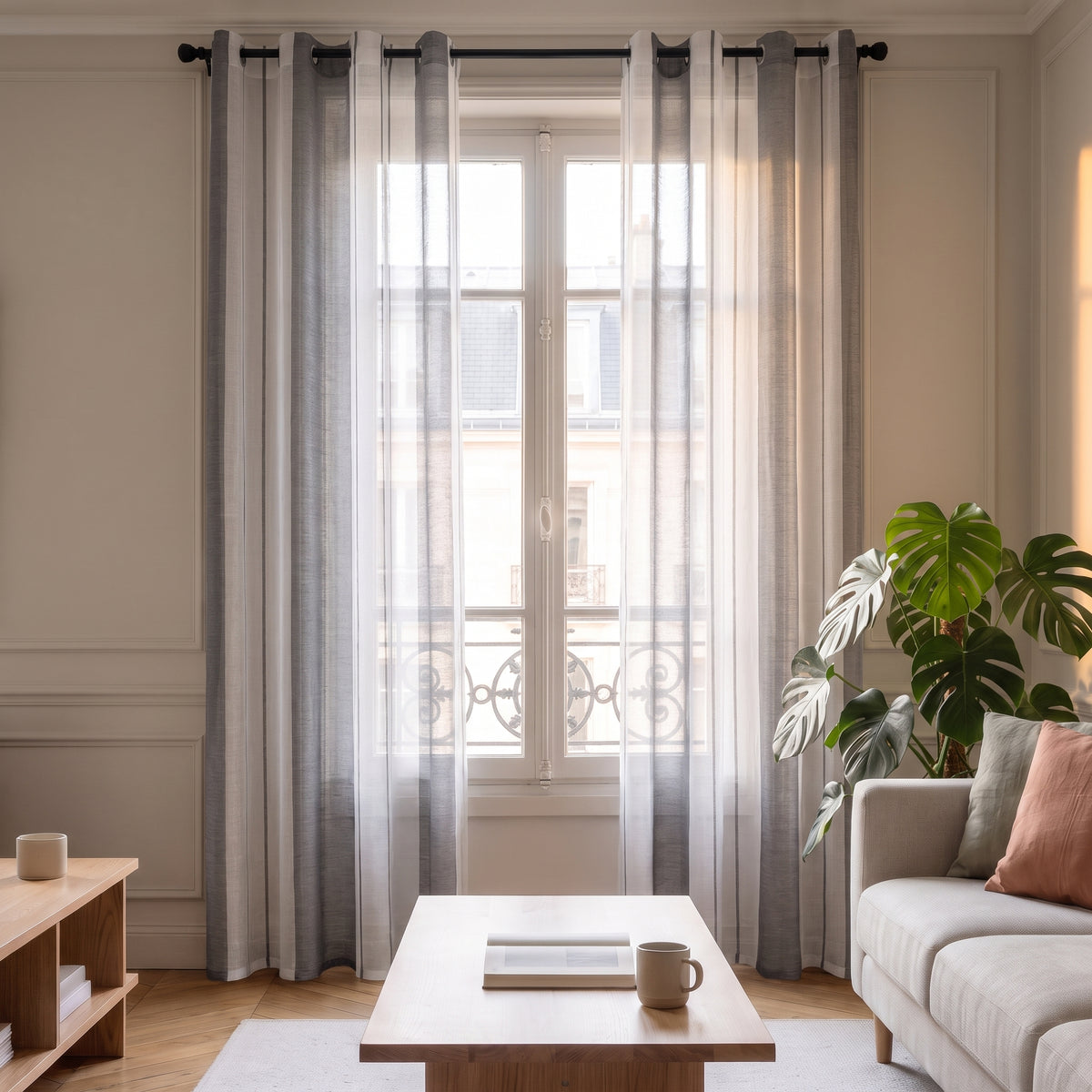 Voilage rayé gris et blanc ouvert de chaque côté de la fenêtre, le jour entre dans le salon
